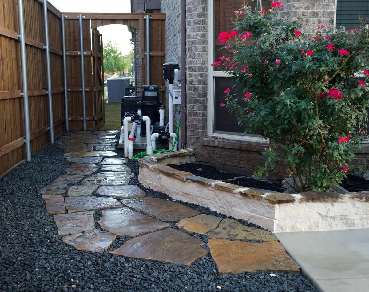 side yard with natural stone pathway, gravel border, and raised flower bed built through expert paver walkway installation in Fort Worth, TX