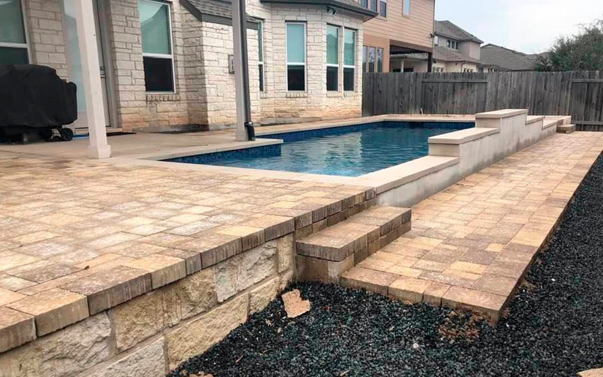 Backyard pool with stone paver deck and raised wall built with outdoor living designs in Fort Worth, TX