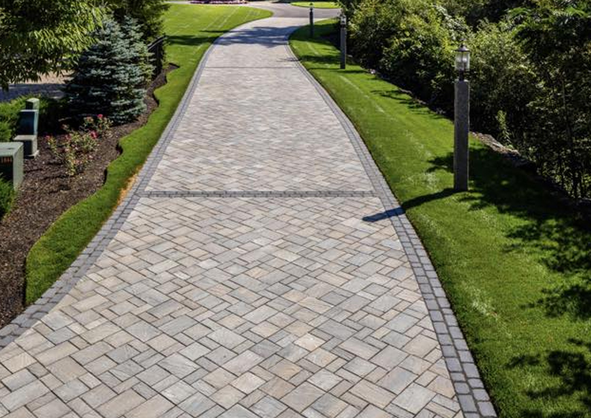 long stone driveway with herringbone paver pattern and trimmed green lawns after professional driveway installation in Fort Worth, TX