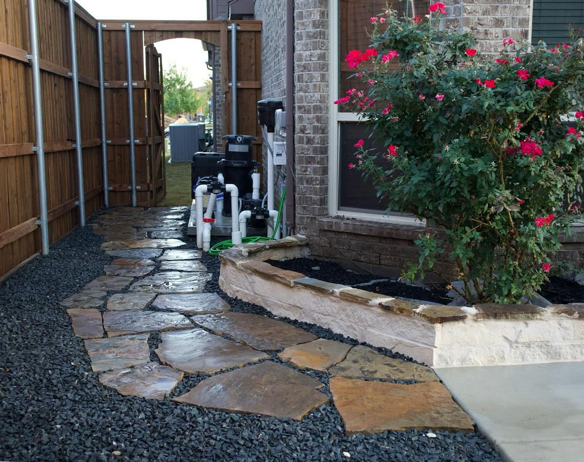 side yard with natural stone pathway, gravel border, and raised flower bed built through expert paver walkway installation in Fort Worth, TX