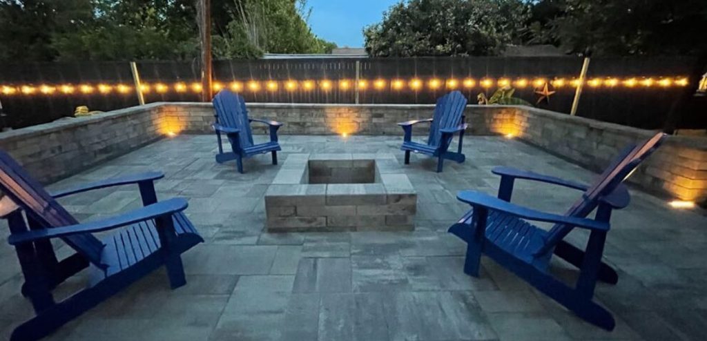 modern backyard patio with stone fire pit, blue chairs, and lighting, featuring Fireplace Backyard Ideas for relaxing outdoor evenings in Fort Worth, TX