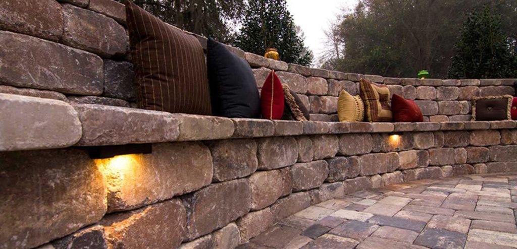 Holistic Patio Hardscaping Services in Fort Worth, TX - Holistic Patio Retaining Wall with Seating Ideas Header stone retaining wall with built-in seating, accent pillows, and lighting, showcasing Retaining Wall with Seating Ideas for cozy outdoor spaces in Fort Worth, TX