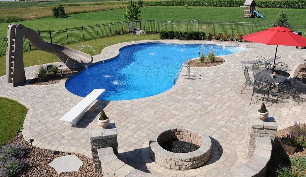Holistic Patio Hardscaping Services in Fort Worth, TX - Outdoor Fire Pit Ideas That Warm Up Your Backyard in Denton County c2 Outdoor fire pit beside a paver pool deck with curved seating walls, showcasing outdoor fire pit ideas for family-friendly backyard designs