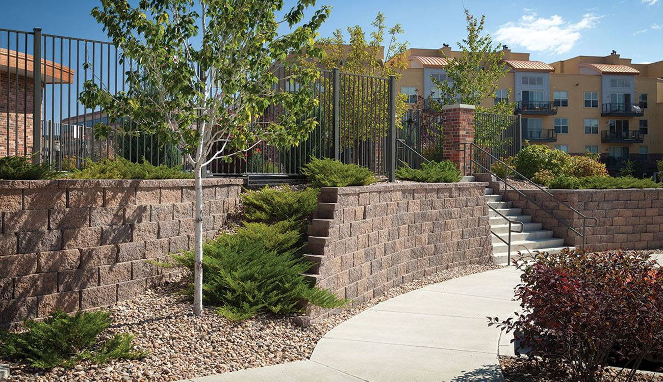 Retaining wall ideas featuring a multi-level stone wall with built-in steps and metal railing for a landscaped outdoor space.
