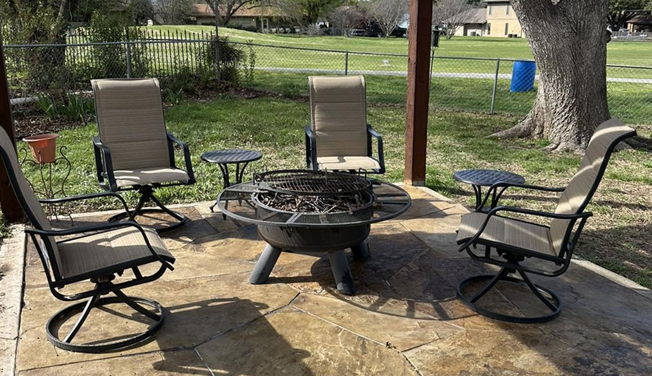 Holistic Patio Hardscaping Services in Fort Worth, TX - Holistic Patio Decor Ideas Circular stone patio features four swivel chairs surrounding a fire pit under a shaded outdoor structure.